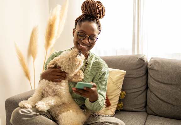 a woman sitting on a couch playing with her dog while holding a remote control at The Walker Virginia Center in Glen Allen, VA