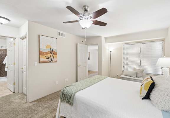 A bedroom with a bed, a ceiling fan, and a painting on the wall.