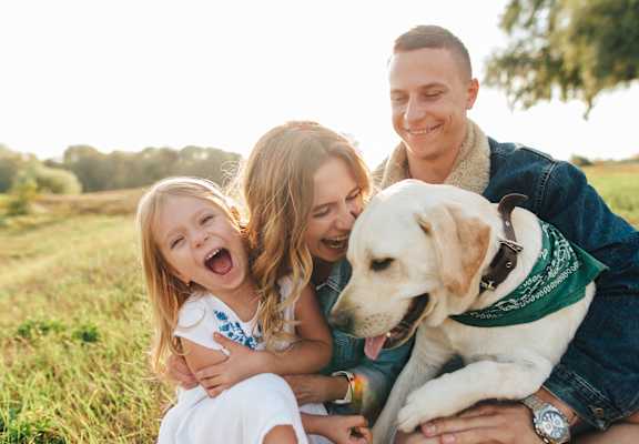 A family of three is sitting on the grass with a dog.