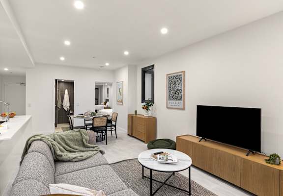 A modern living room with a grey sofa, a black TV, and a dining table with chairs.