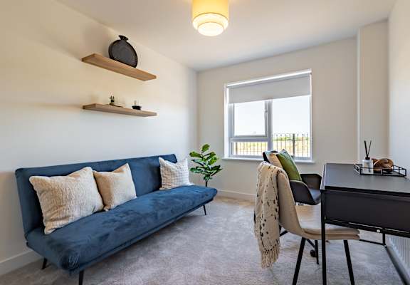 A blue couch with pillows and a blanket sits in a room with a desk and chair.