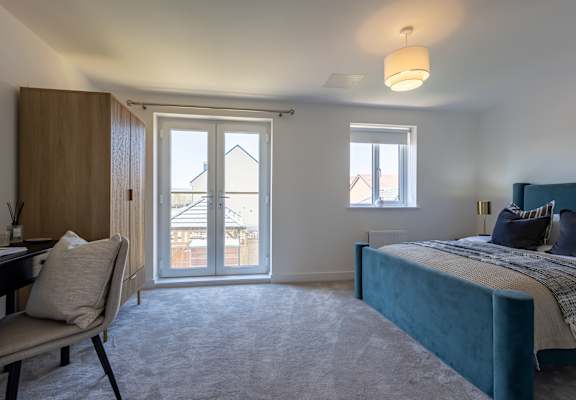 A bedroom with a bed, desk, chair, and a window with a view of a house.