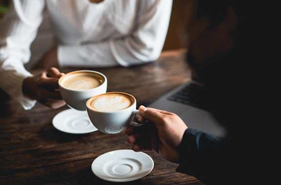 two people holding coffee cups while sitting at a table