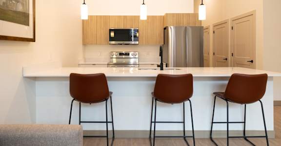 A kitchen with a refrigerator, microwave, and two chairs.