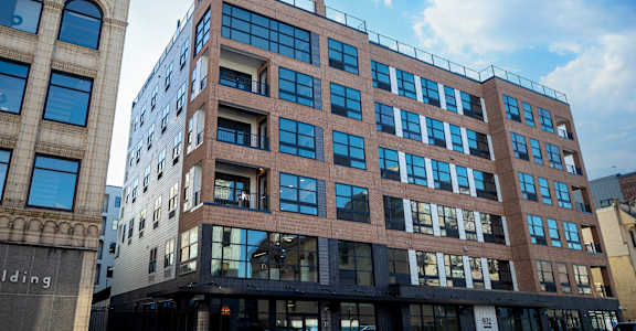 A modern building with a glass facade stands next to an older building with arched windows at The Gallery Apartment Homes Apartments, Allentown, PA, 18101