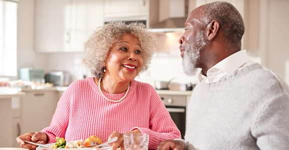 An older couple enjoying a meal together in a brightly lit kitchen.
