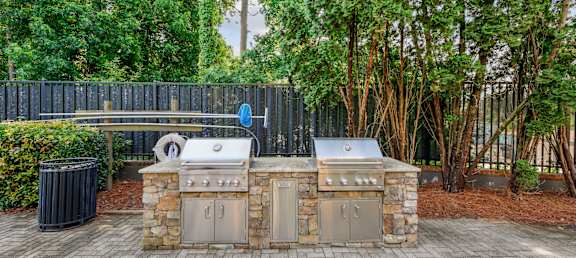 A stone and metal outdoor kitchen with a grill and sink.