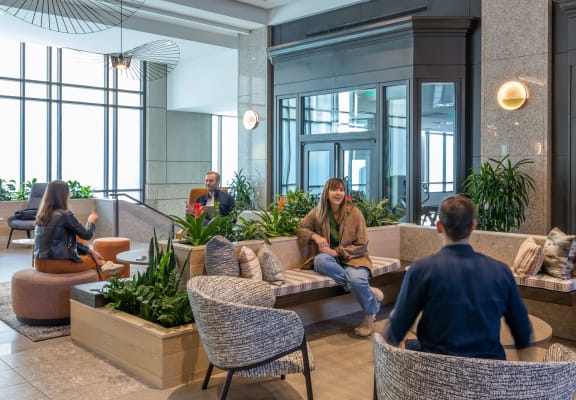 a group of people sitting in a lobby with furniture and plants