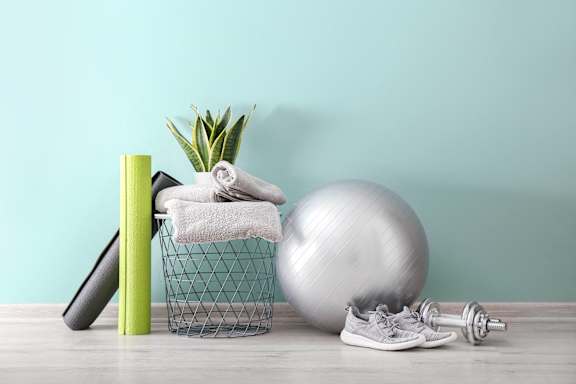 A fitness setup with a ball, a basket with towels, a yoga mat, and a pair of sneakers.