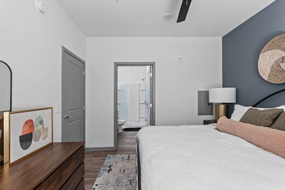 A bedroom with a bed, a painting, a rug, a ceiling fan, and a door.