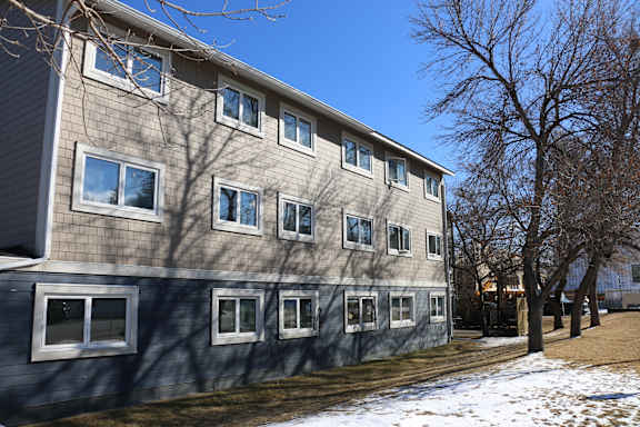 A grey building with white windows and a tree in front.