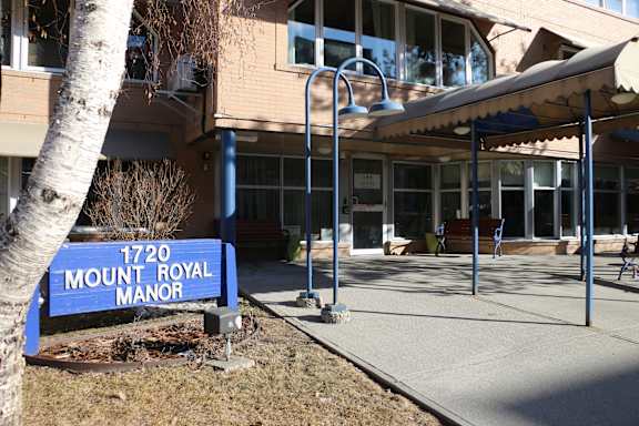 A blue sign that says Mount Royal Manor stands in front of a building.