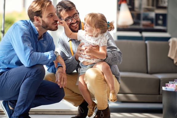 a man in a blue shirt and khaki pants kneels down to kiss a little girl