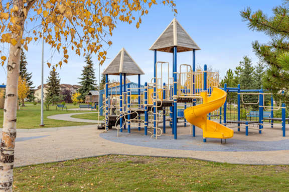 A playground with a yellow slide and a wooden structure.