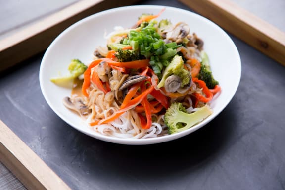 a bowl of noodles with vegetables on a wooden tray