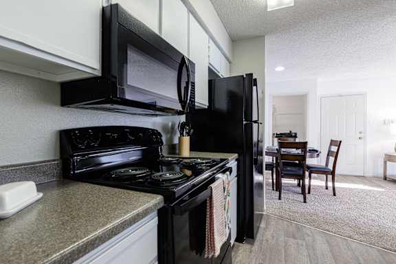 A kitchen with a stove and microwave, adjacent to a dining room with a table in the Skyler Ridge Apartments model unit.