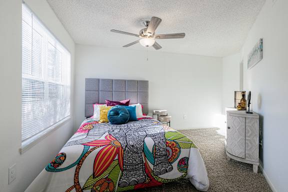 A bedroom in the model unit at Skyler Ridge Apartments with a bed and ceiling fan.