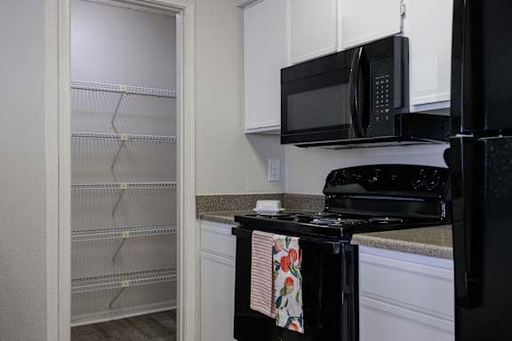 A kitchen view in the model unit at Skyler Ridge Apartments, showcasing white cabinets, a black stove, and a microwave.