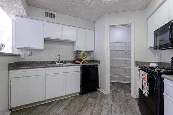 A kitchen in the model unit at Skyler Ridge Apartments, featuring white cabinets, a black dishwasher, and a sink.