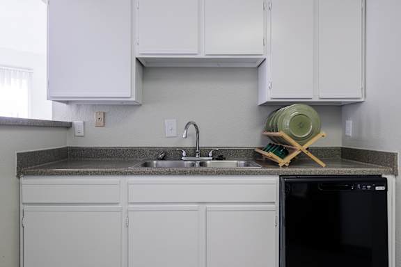 A kitchen view in the model unit at Skyler Ridge Apartments, showcasing white cabinets, a black dishwasher, and a sink.