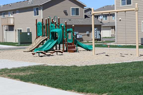 A playground with a green slide and a brown wooden structure.