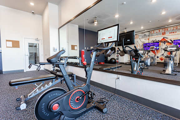 A spin bike is in the foreground of a gym with mirrors and other exercise equipment.