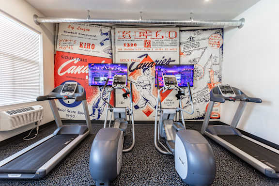 A gym with treadmills and a wall with posters.