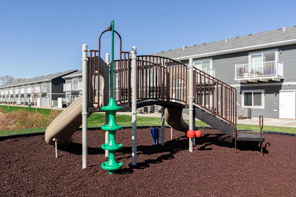 A playground with a green and brown slide and a red ball.