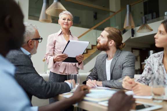 A woman is presenting a report to a group of people in a meeting room.