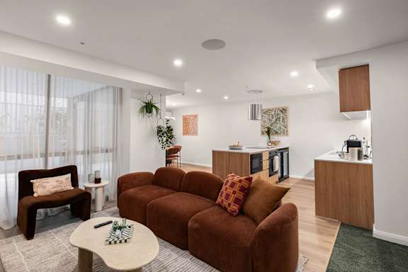 A living room with a brown couch and a small table with a plant on it.