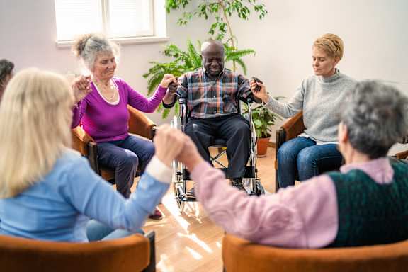 A group of elderly people are sitting in a circle and holding hands.
