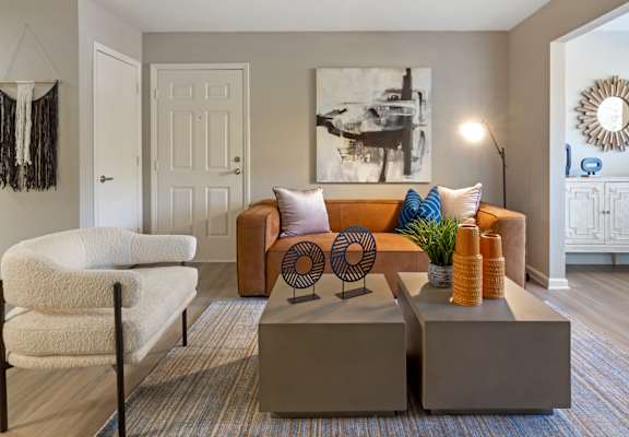A living room with a white chair, a brown couch, and a large painting on the wall.
