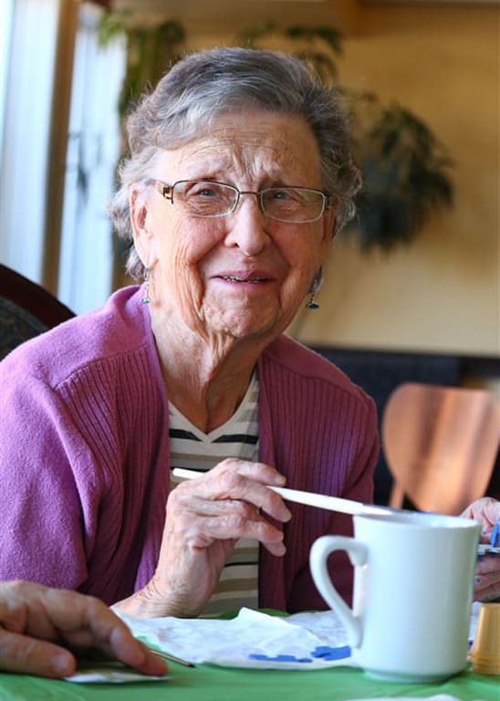 an old woman sitting at a table with a cup of coffee