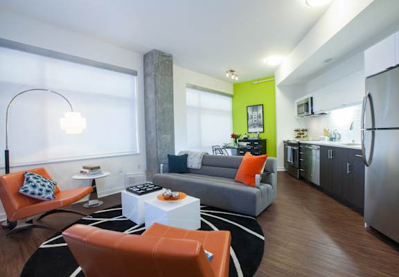 A modern living room with a grey couch, orange chairs and a black and white rug.