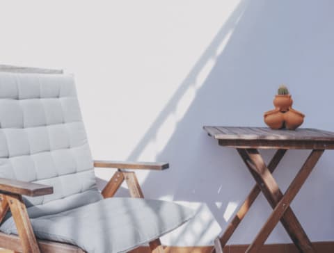 Wood Patio Chair with Grey Cushion Next to Wood Folding Table with Pots and Cacti