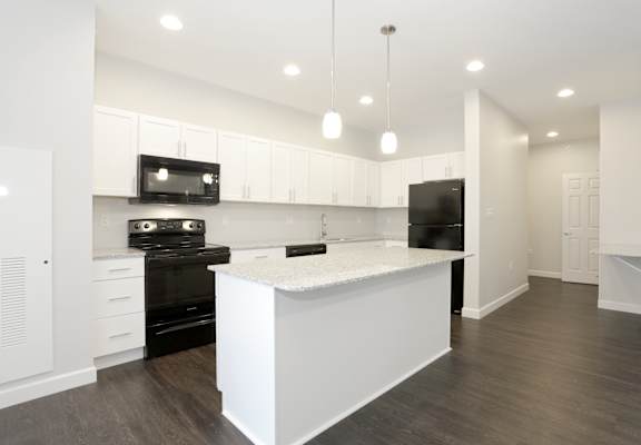 A modern kitchen with a white island and black appliances at Promenade at Founders Square Apartments in Indianapolis, IN