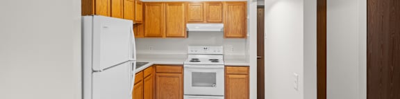 A white refrigerator is in a kitchen with wooden cabinets.