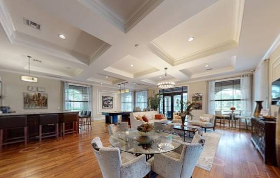 A living room with a grey rug and a brown ottoman.