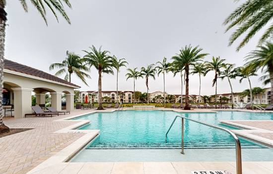 A swimming pool surrounded by palm trees and a building in the background.