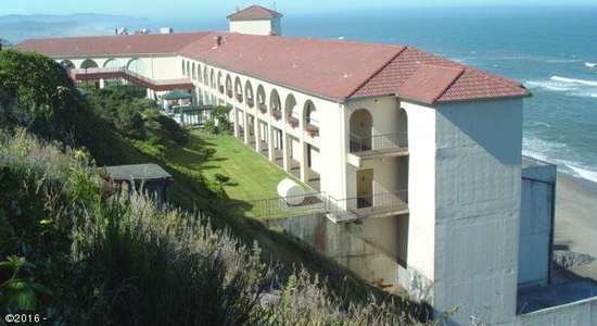 A building with a red roof is situated on a cliff by the ocean.