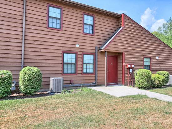 a brown house with a red door and a yard