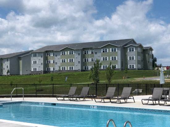 a swimming pool with chairs in front of an apartment building