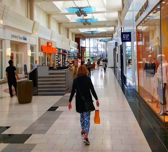 A woman is walking down a spacious hallway in a mall.