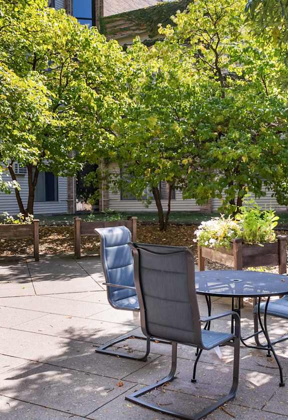 A patio with chairs and a table surrounded by trees.