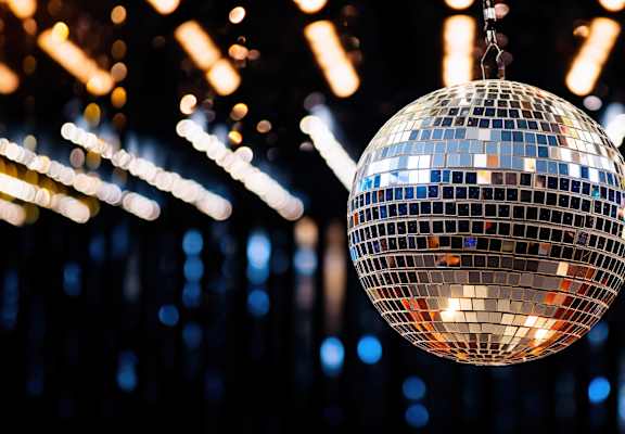A disco ball hanging from the ceiling with lights in the background.
