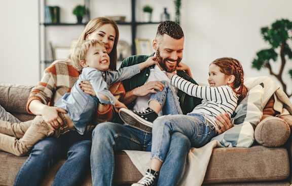 A family of four is sitting on a couch, with two children hugging their parents.