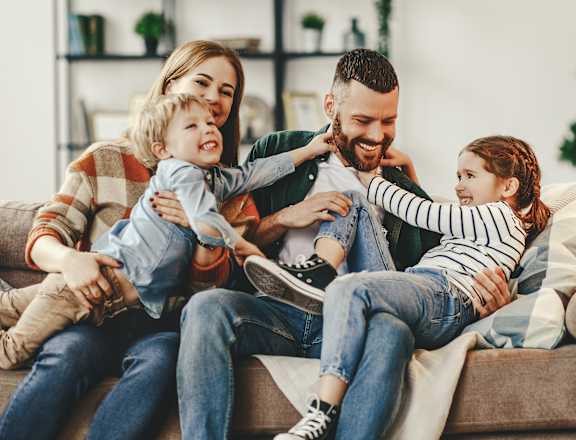 A family of four is sitting on a couch, with two children hugging their parents.