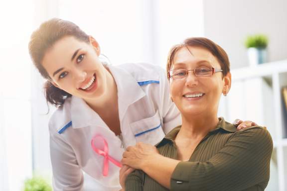 A woman wearing a pink ribbon is hugging another woman.