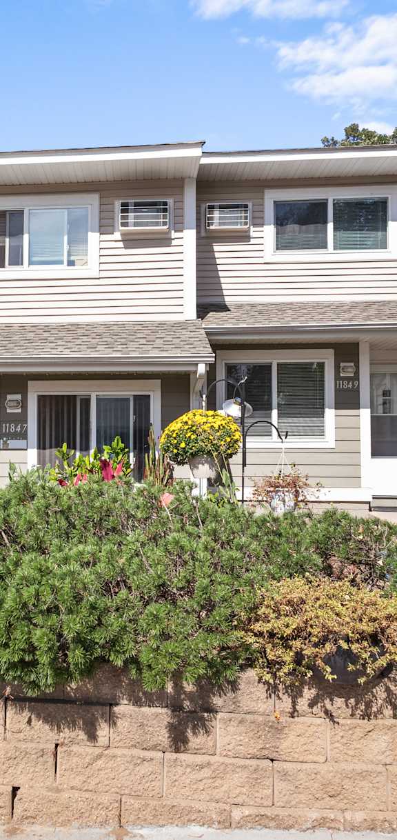 A house with a grey siding and a brown roof with a garden in front.
