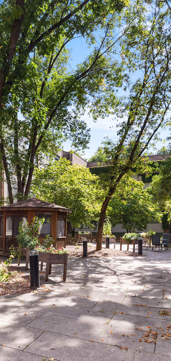 A tree-lined walkway leads to a small pavilion in a courtyard.
